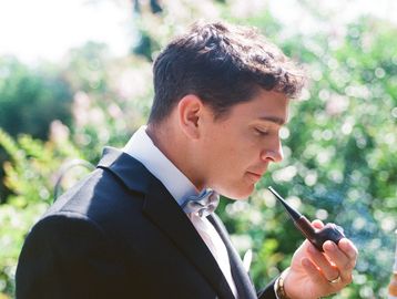 A man in a tuxedo smoking a pipe outdoors.