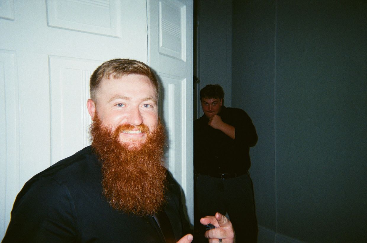 Two men in black shirts posing indoors, one with a large red beard smiling.