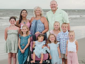 A family group photo on the beach with adults and children smiling.