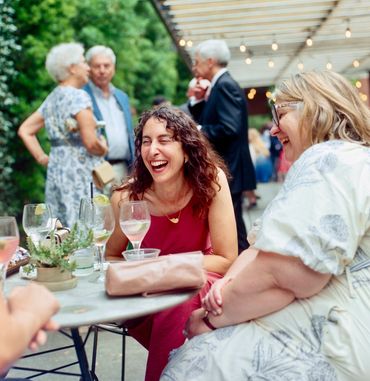 Two women laughing and enjoying drinks at an outdoor gathering for cocktail hour.