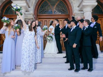 Bride and groom kiss as wedding party cheers outside a church.