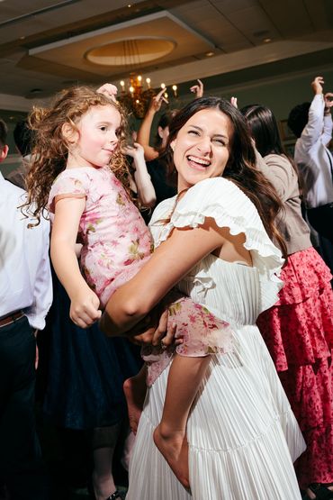 A joyful woman holding a young girl at a lively wedding reception party.