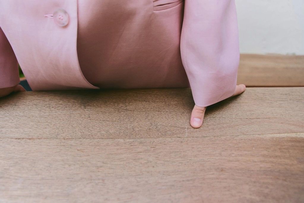 Person in a pink suit pointing at a wooden surface.