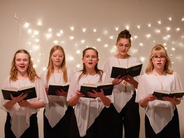 Group of five girls singing with songbooks.