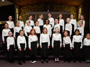Group of girls in matching choir uniforms posing indoors.