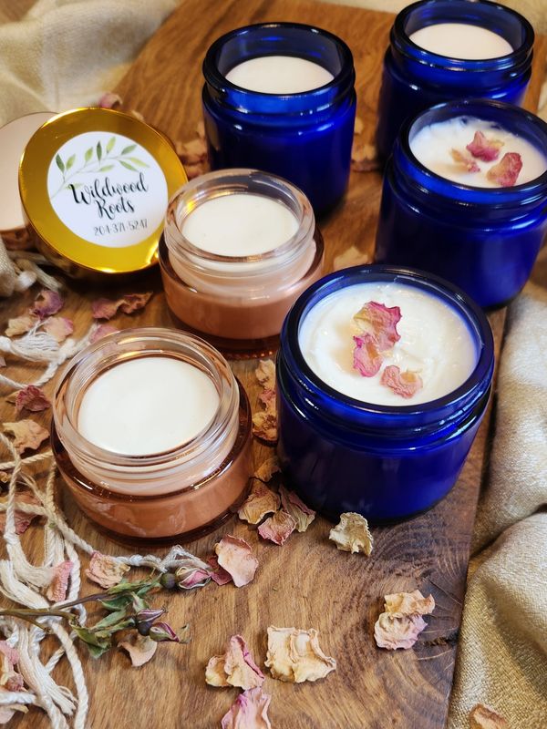 Handmade candles in blue and peach jars with dried rose petals on a wooden board.