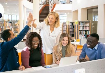 Group of diverse students celebrating with a high five in a library.