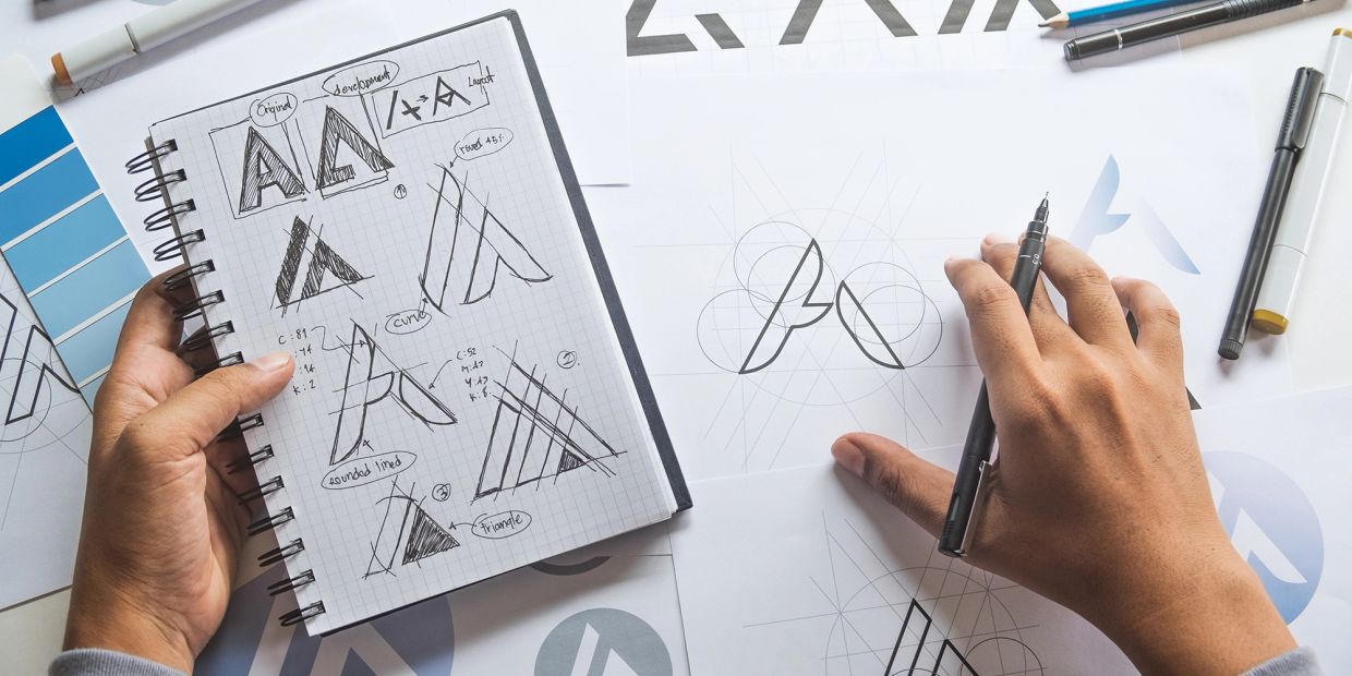 Designing and sketching geometric logo concepts on paper.