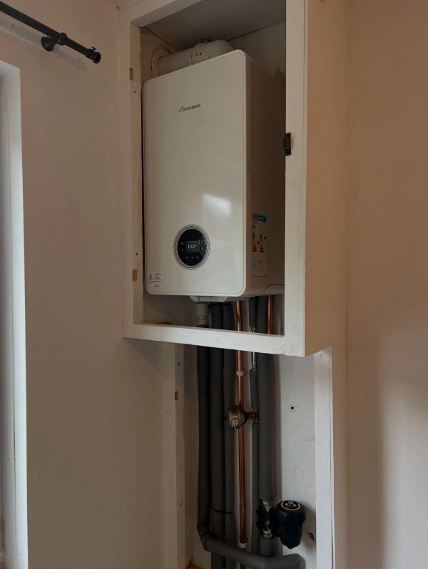 White boiler unit installed in a wall recess with visible pipes.