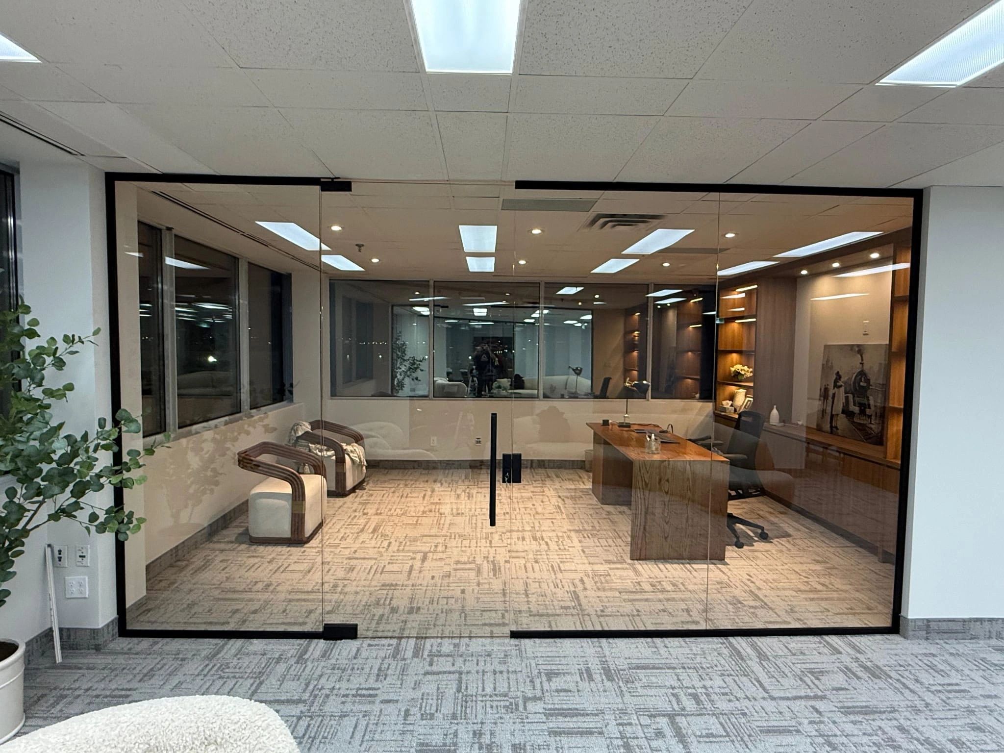 Modern office with glass doors and wooden desk.
