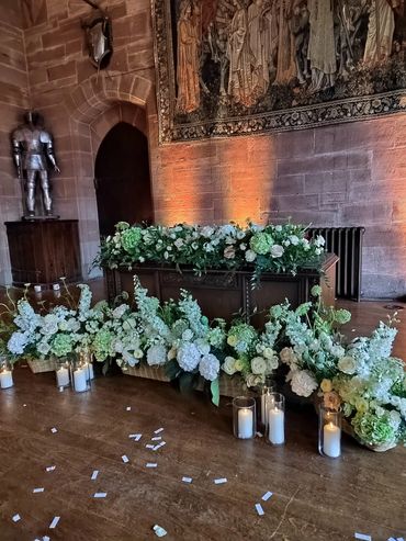 Luxurious ceremony table flowers and candles at peckforton castle. baskets filled with white flowers
