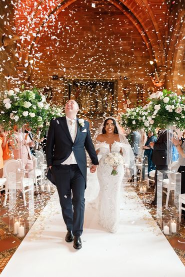 Close up of couple walking down the aisle at castle past tall floral plinths.