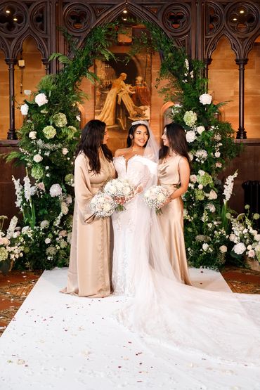 Bride and Bridesmaids in front of floral arch at Peckforton Castle holding Gypsophila bouquets