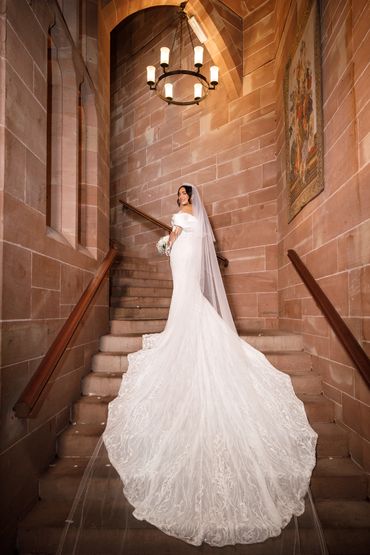 Bride posing with her bouquet filled with roses on staircase in castle. Her dress is long tailed.