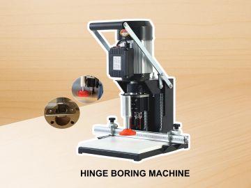 A hinge boring machine with a motor and adjustable base on a wooden surface.