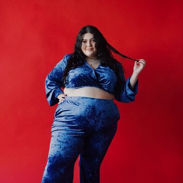 @duhmiii standing in front of red backdrop blue velvet croptop,matching pants,pulling hair left hand