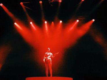 Musician St Vincent standing on stage with guitar on red platform with red stage lights shining down