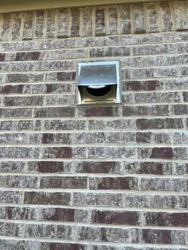 Metal vent on a brick wall with a flap partially open.