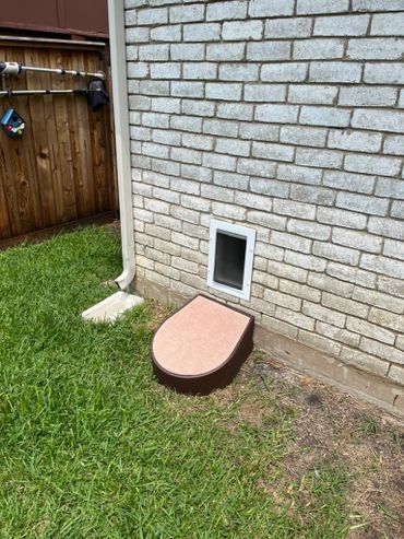 Small pet door with a step outside a brick house wall.
