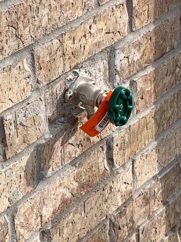 Outdoor water faucet with a green handle on a brick wall.