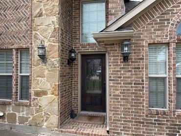 Brick and stone house entrance with dark wooden door and three lantern-style lights.