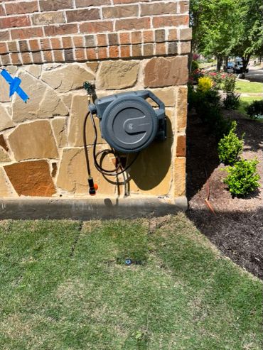 Wall-mounted garden hose reel on a stone wall near a lawn.
