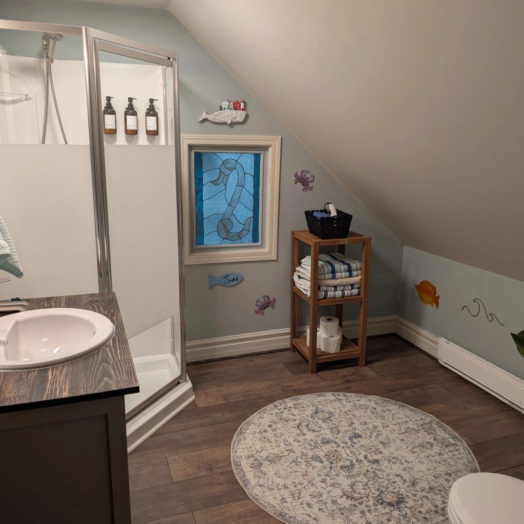 Cozy bathroom with nautical decor and wooden flooring under a slanted ceiling.