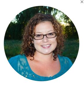 Smiling woman with glasses in a teal top outdoors.