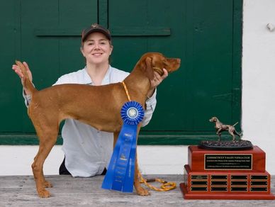 Person proudly posing with a dog and a trophy.