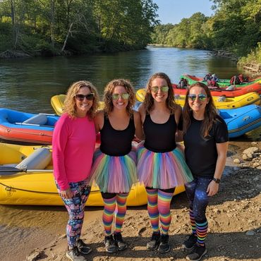 Four woman wearing colorful tights and tutus pose in front of rafts lined up on the river bank