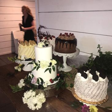 A table with four decorated cakes and floral decorations indoors.