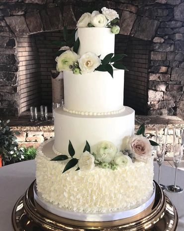 Elegant three-tier white wedding cake with floral decorations and greenery.