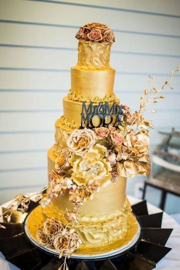 Elegant gold four-tier wedding cake with floral decorations and Mr & Mrs topper.