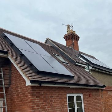 Solar panels installed on sloped roofs of a brick house under cloudy sky.