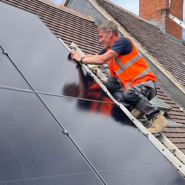 Technician installing solar panels on a sloped roof under a blue sky.