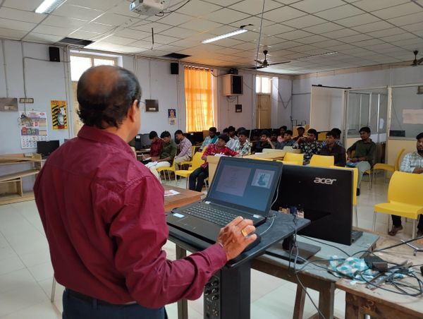 A teacher giving a lecture to students in a classroom with computers.