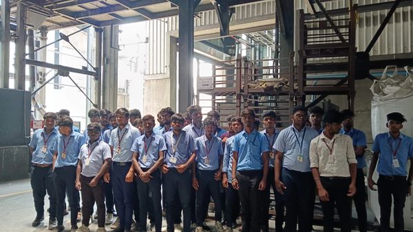 Group of young men in blue shirts standing inside an industrial building.