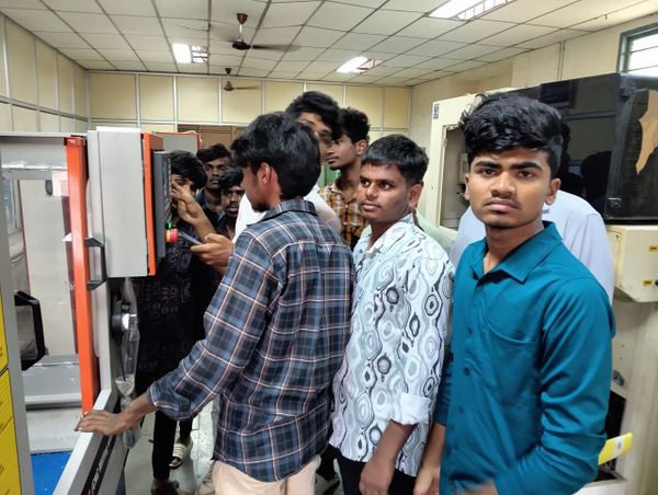 A group of young men gathered around a machine in a classroom or lab setting.