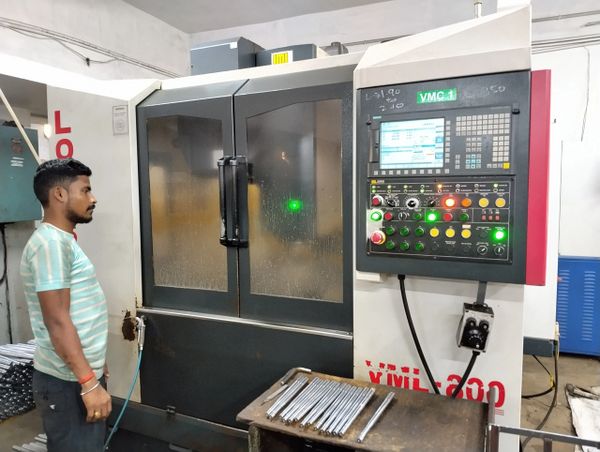Man operating a CNC machine in a workshop with metal rods on a table.