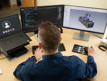 Man working on computer coding and 3D modeling with three monitors.