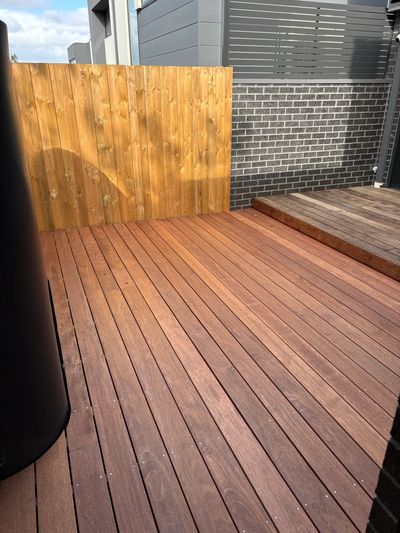 A clean wooden deck with a small step and a wooden fence beside a gray brick wall.