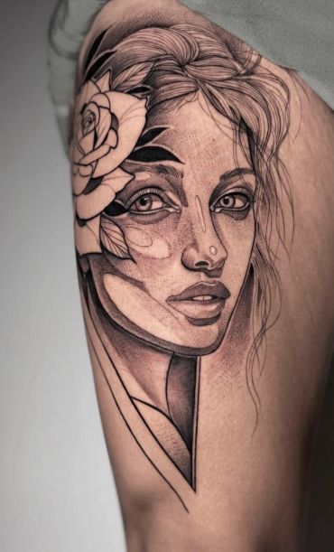Black and grey illustrative woman's face tattoo featuring expressive eyes, detailed linework, soft shading, and floral accents.