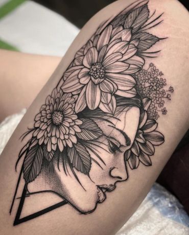 Black and grey tattoo of a woman's face surrounded by detailed flowers and leaves.