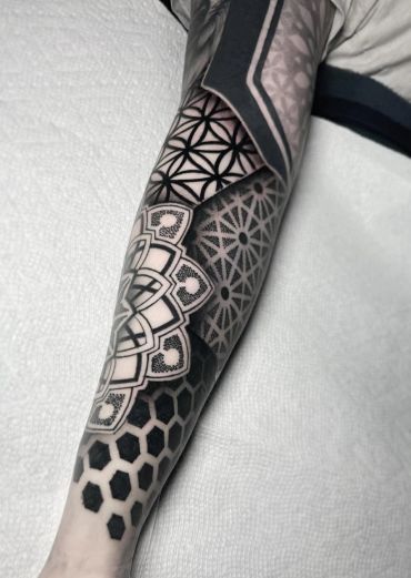 Blackwork geometric forearm tattoo featuring intricate mandala patterns, bold black shading, precise linework, and negative space designs.