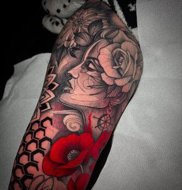 Black and grey upper arm tattoo featuring a woman's profile, detailed roses, geometric blackwork patterns, and bold red accents.