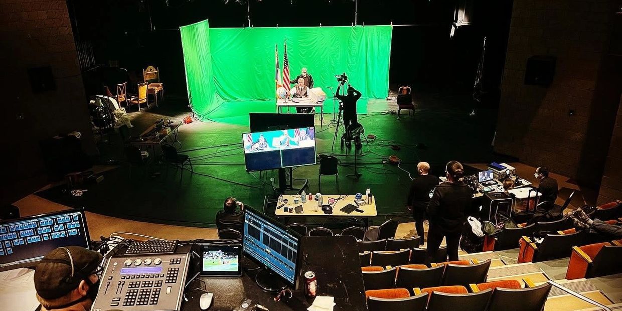 Green screen studio setup with a crew filming a person at a desk.