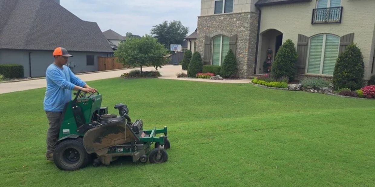 Man mowing lawn with a green mower.