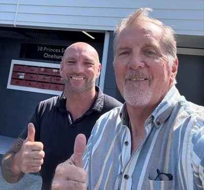 Two men smiling and giving thumbs up outdoors.