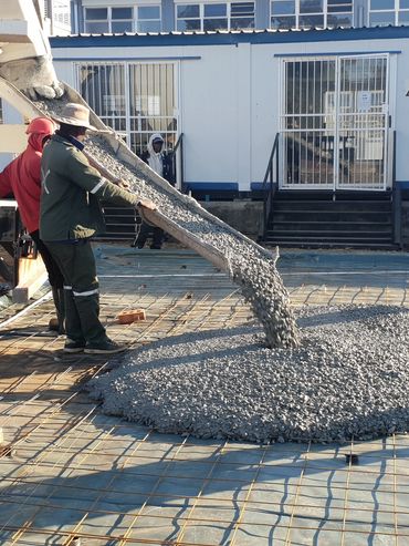 Workers pouring concrete from a cement mixer onto a prepared surface.
