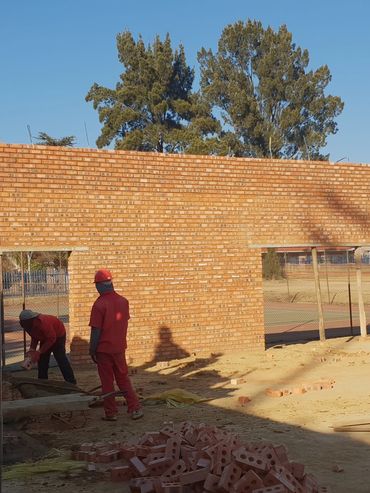 Workers building a brick wall under clear blue sky.